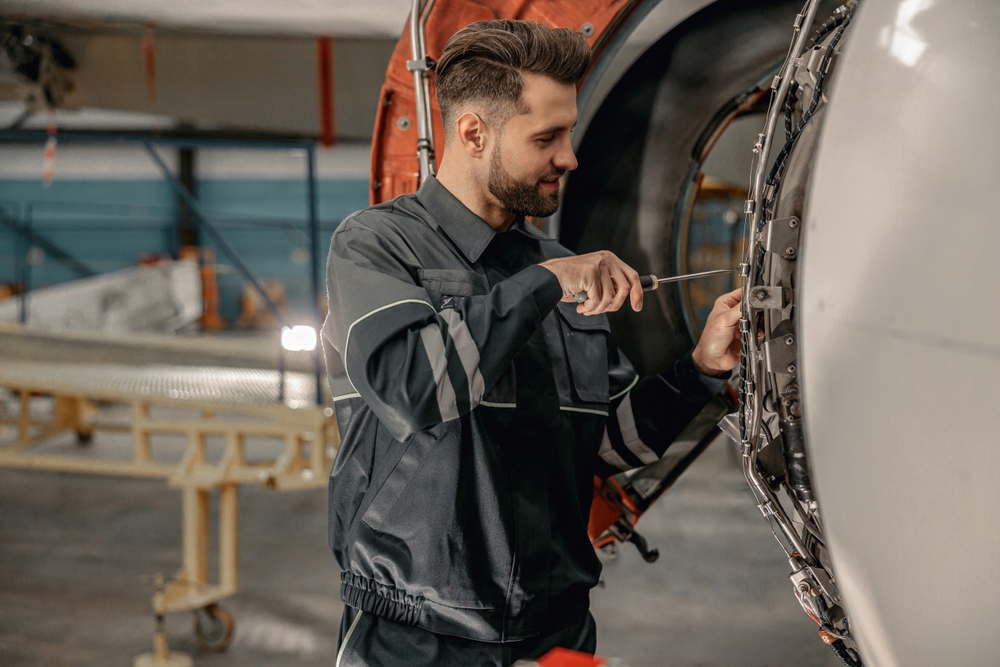 Smiling,man,airline,maintenance,technician,using,screwdriver,while,repairing,airplane